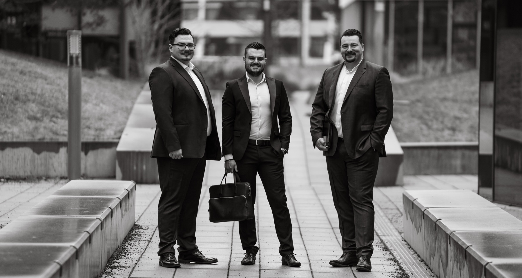 Schwarzweiß-Teamportrait dreier Männer in Anzügen